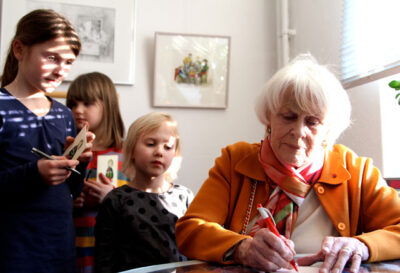 Die Künstlerin Ilon Wikland mit Kindern beim Signieren in der Ausstellung “Über Tisch und Bänke”.