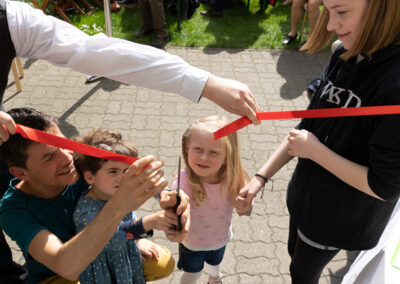 Anlässlich der Ausstellungseröffnung “Von Anna Humpelhexe bis Zacharias Zappelbein” im LesArt-Garten zerschneiden Kinder feierlich rotes Band im Eingangsbereich.