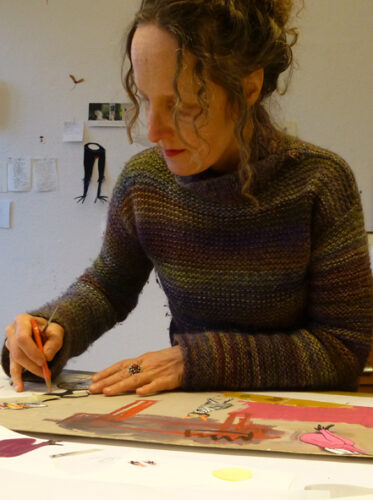 Illustratorin Stefanie Harjes beim Gestalten ihre Erzählbildes. Sie trägt lockiges zusammengebundenes, braunes Haar, einen Strickpullover und ist über ihr Bild gebeugt, auf dem sie mit Buntstift zeichnet.