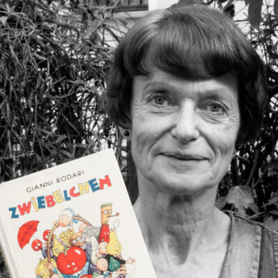 Edda Eska hält das Buch “Zwiebelchen” von Gianni Rodari neben ihr Gesicht.