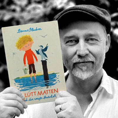 Frank Kurt Schulz hält das Buch “Lütt Matten und die weiße Muschel” von Benno Pludra neben sein Gesicht.