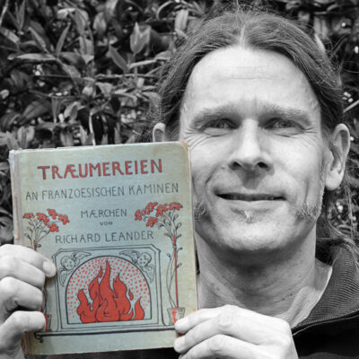 Götz Drope hält das Buch “Träumereien an französischen Kaminen” von Richard Leander neben sein Gesicht.