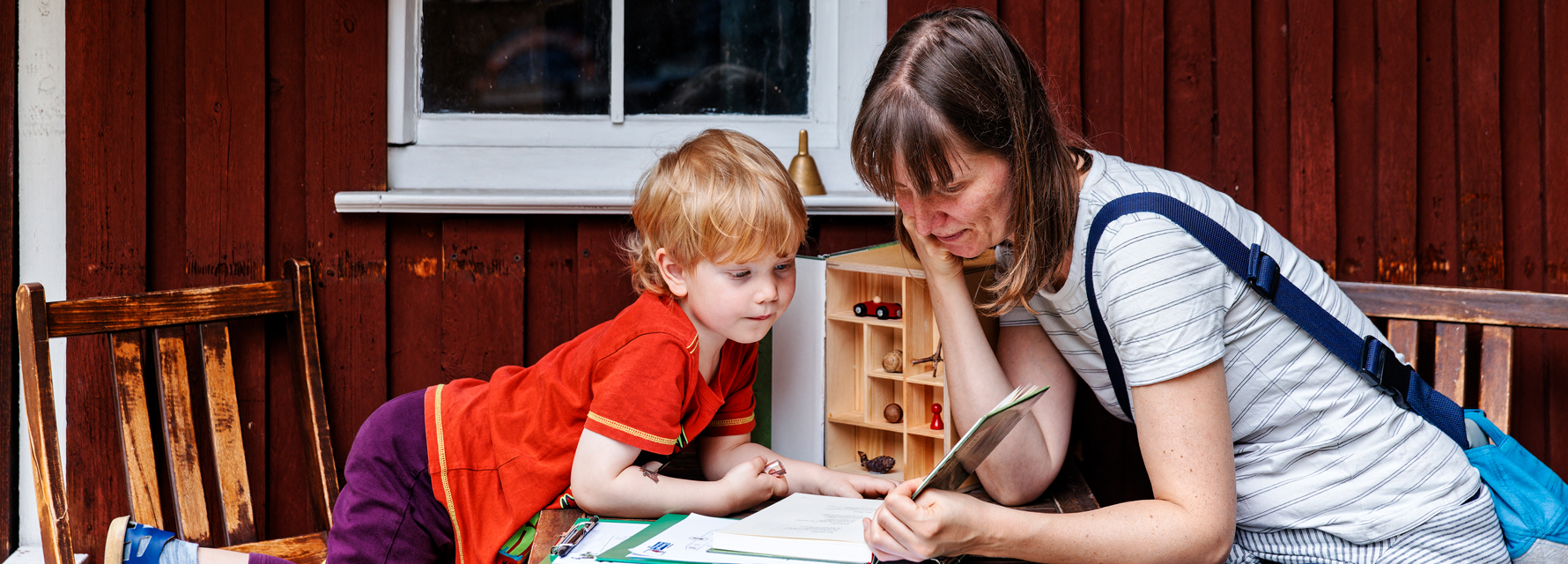 Mutter und Kind sitzen vorm Gartenhäuschen bei LesArt und lesen in einem Buch